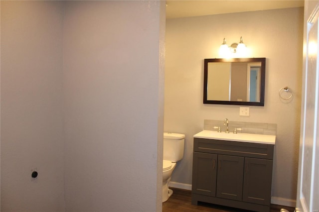 bathroom featuring toilet, baseboards, wood finished floors, and vanity