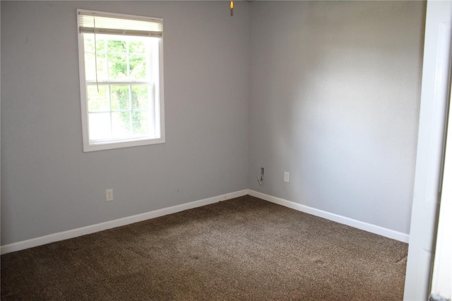 spare room with baseboards and dark colored carpet