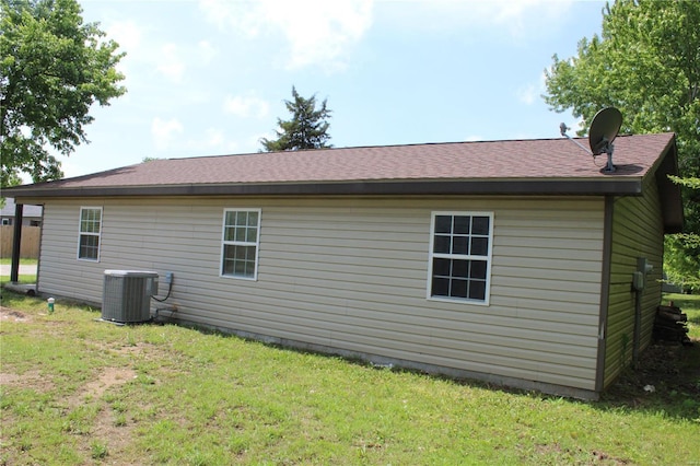 view of home's exterior with central AC unit, a yard, and a shingled roof