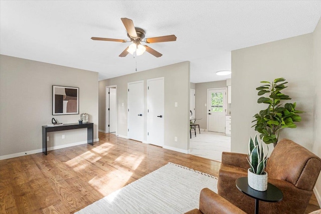 living area with baseboards, a ceiling fan, and light wood finished floors