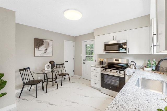kitchen featuring a sink, baseboards, marble finish floor, stainless steel appliances, and white cabinetry