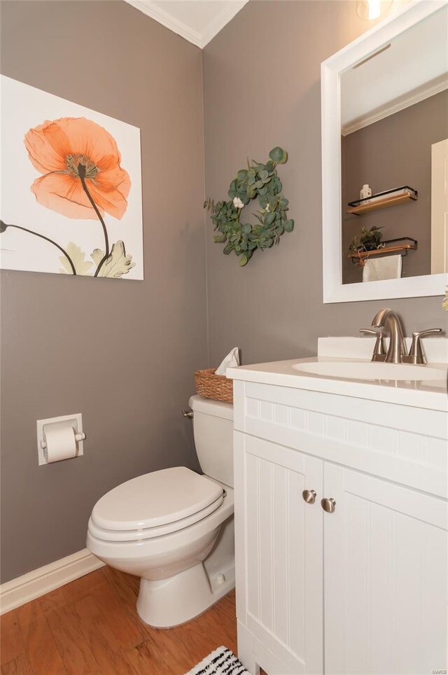 bathroom featuring vanity, ornamental molding, wood finished floors, toilet, and baseboards