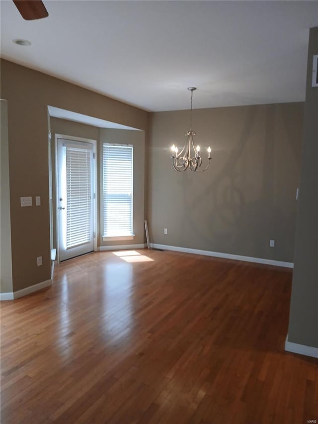 unfurnished dining area with baseboards, ceiling fan with notable chandelier, and wood finished floors