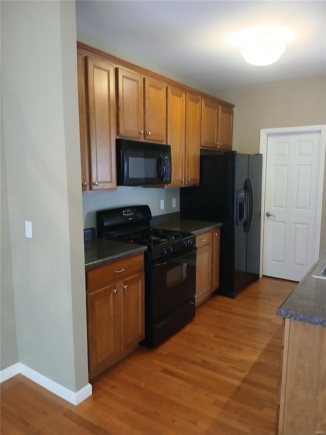 kitchen featuring light wood-style floors, baseboards, brown cabinetry, and black appliances