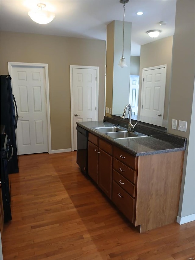 kitchen with dark countertops, a sink, light wood-style flooring, black dishwasher, and baseboards