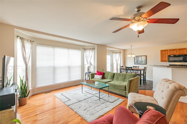 living area featuring visible vents, ceiling fan with notable chandelier, and light wood-type flooring