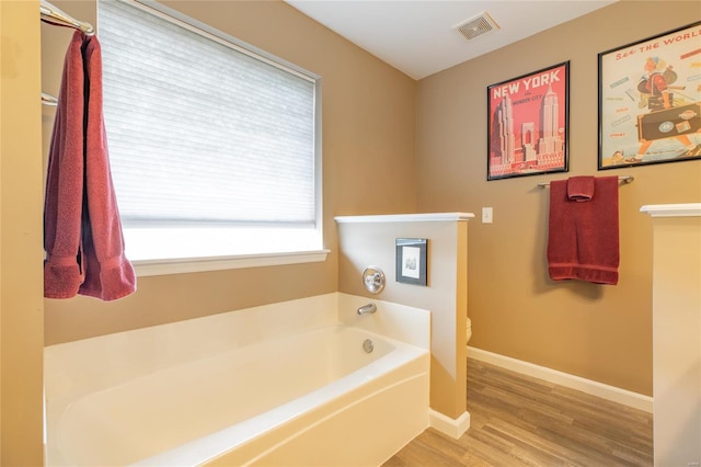 bathroom featuring visible vents, wood finished floors, toilet, baseboards, and a bath