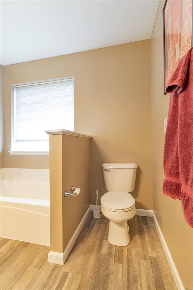 bathroom with toilet, baseboards, wood finished floors, and a garden tub