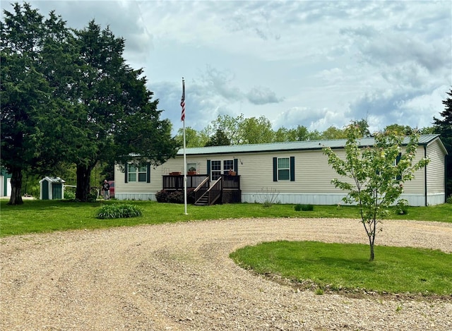 manufactured / mobile home featuring a front lawn, a deck, curved driveway, a shed, and an outbuilding