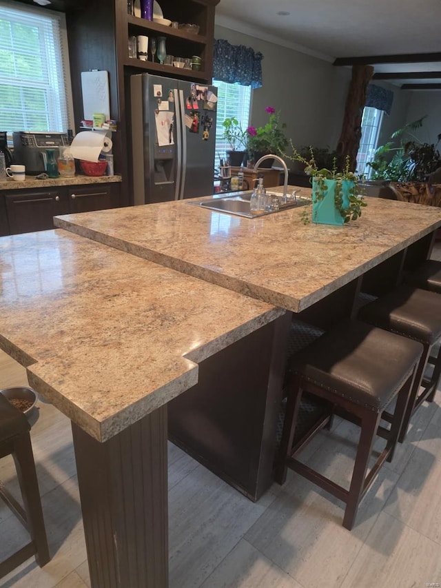 kitchen with a large island with sink, a sink, stainless steel fridge with ice dispenser, light countertops, and a breakfast bar