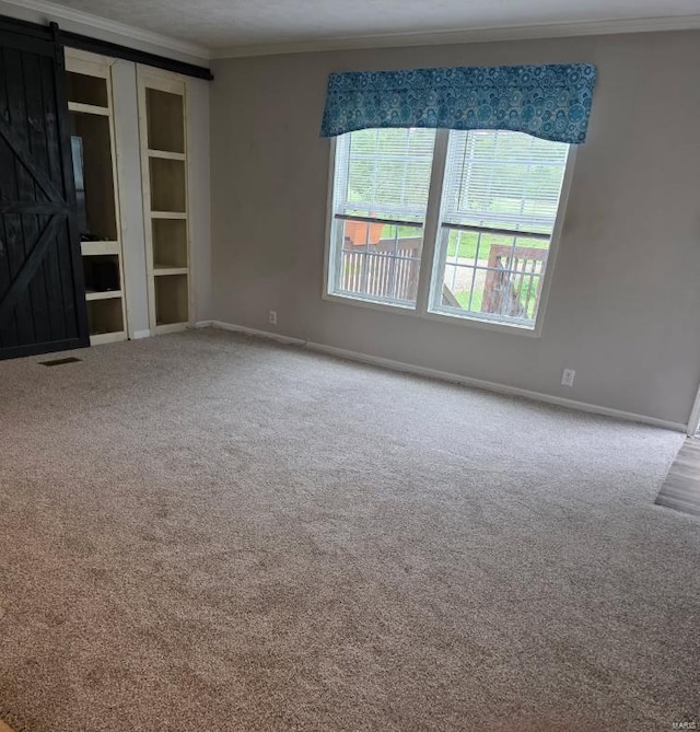 carpeted spare room featuring crown molding, baseboards, visible vents, and a barn door