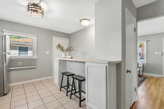 kitchen featuring baseboards, plenty of natural light, freestanding refrigerator, and a kitchen bar