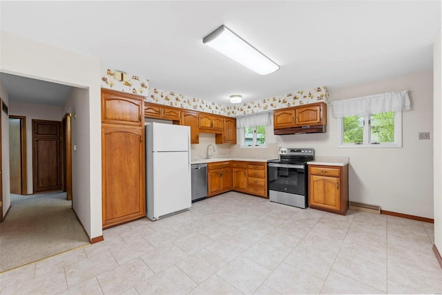 kitchen featuring brown cabinetry, light countertops, under cabinet range hood, a sink, and appliances with stainless steel finishes