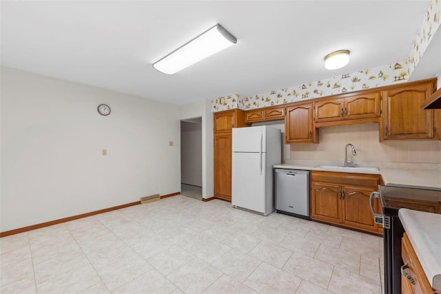 kitchen with range with electric cooktop, brown cabinets, dishwasher, a sink, and freestanding refrigerator