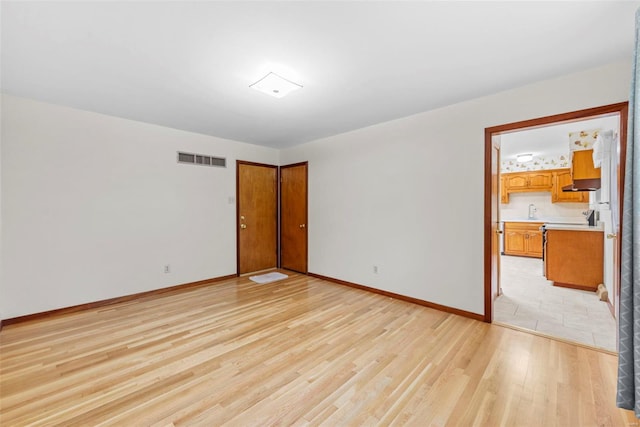 empty room featuring baseboards, visible vents, a sink, and light wood-style floors