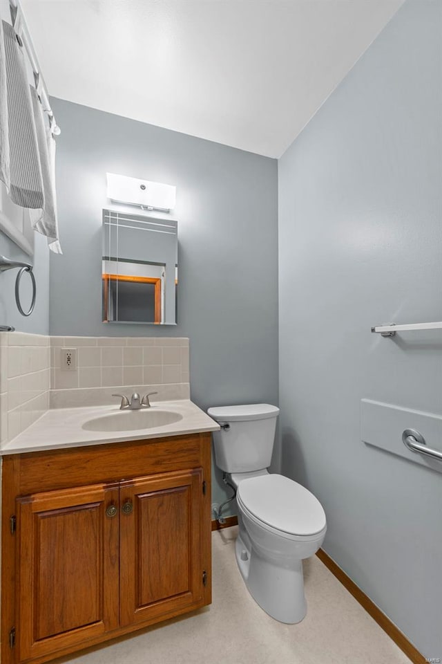 half bathroom with vanity, baseboards, backsplash, and toilet