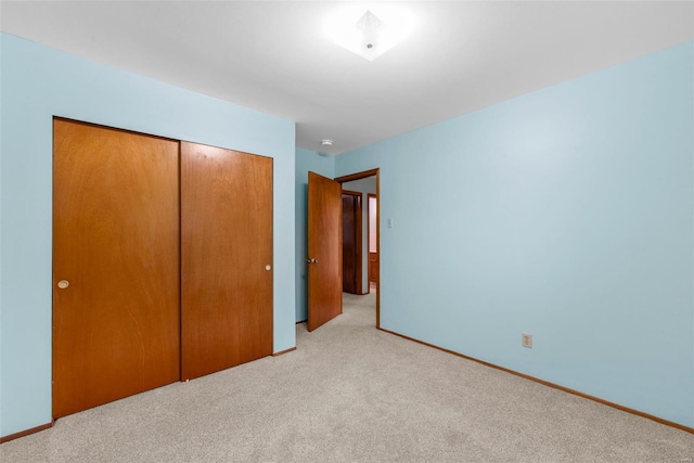 unfurnished bedroom with baseboards, light colored carpet, and a closet