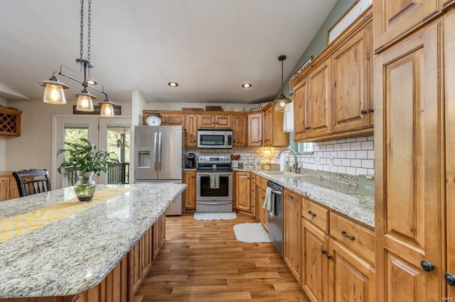 kitchen with light stone counters, a sink, light wood finished floors, stainless steel appliances, and backsplash