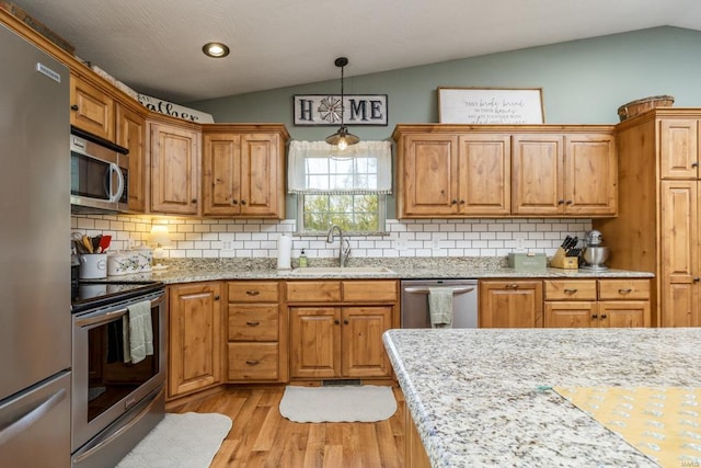 kitchen with a sink, appliances with stainless steel finishes, vaulted ceiling, and light wood finished floors