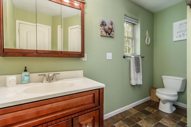 bathroom featuring baseboards, stone finish floor, vanity, and toilet