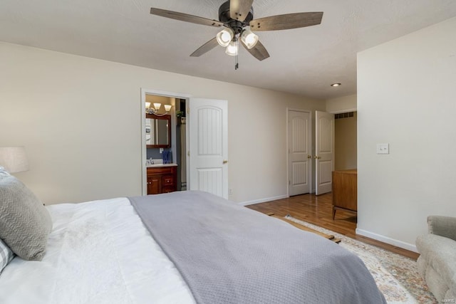 bedroom featuring connected bathroom, a ceiling fan, baseboards, wood finished floors, and visible vents