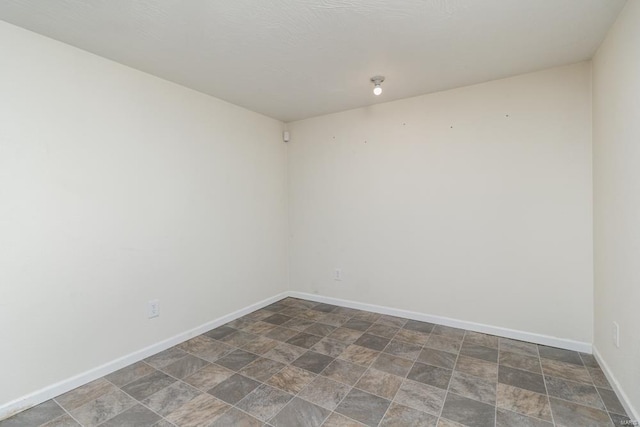 unfurnished room with baseboards and stone finish floor