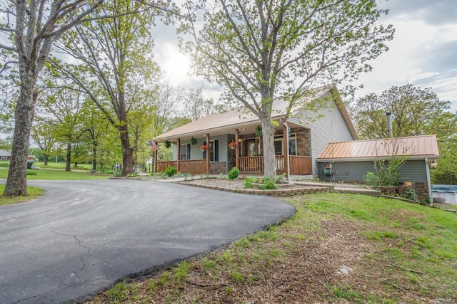view of front of home with covered porch, metal roof, stone siding, and aphalt driveway