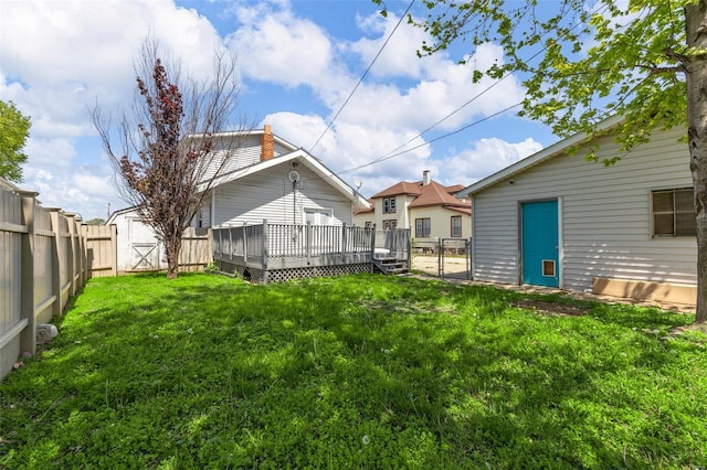 view of yard with an outdoor structure, a wooden deck, a fenced backyard, and a shed