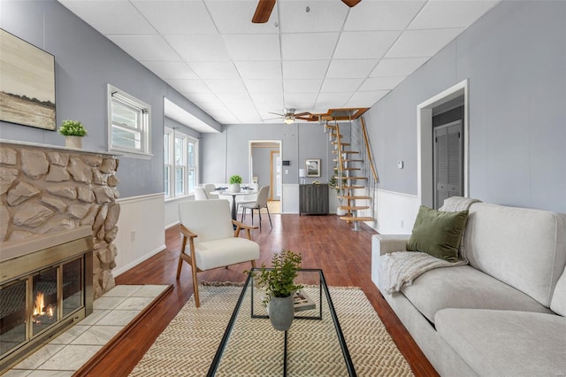 living area featuring stairway, a fireplace, a ceiling fan, and wood finished floors