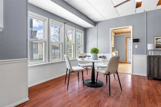 dining space featuring ceiling fan, wood finished floors, and a wainscoted wall