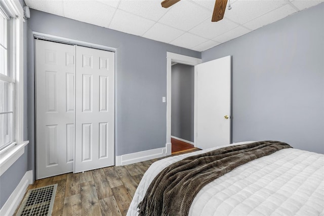 bedroom with a paneled ceiling, a ceiling fan, baseboards, wood finished floors, and a closet