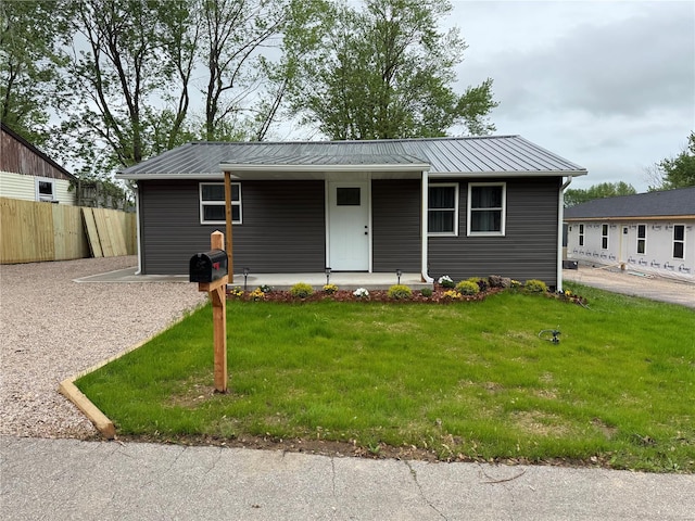 ranch-style house with covered porch, fence, metal roof, and a front lawn