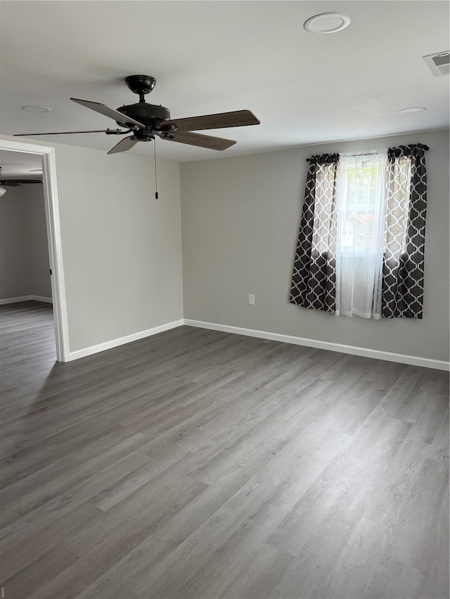 unfurnished room featuring visible vents, a ceiling fan, baseboards, and dark wood finished floors