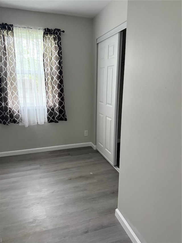 unfurnished bedroom with baseboards, wood finished floors, and a closet