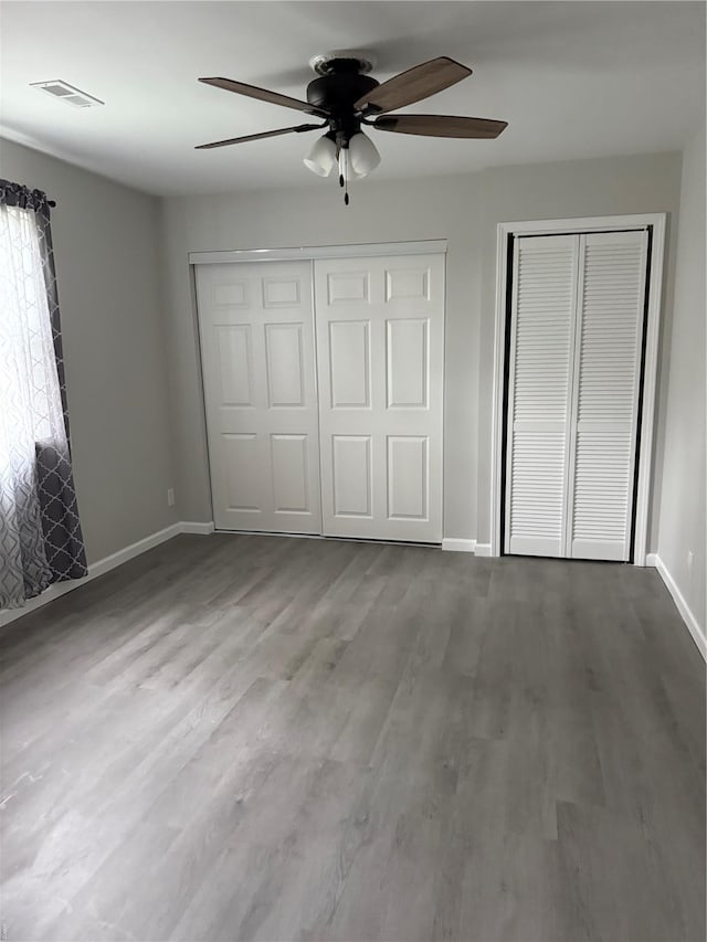 unfurnished bedroom featuring a ceiling fan, baseboards, visible vents, and wood finished floors