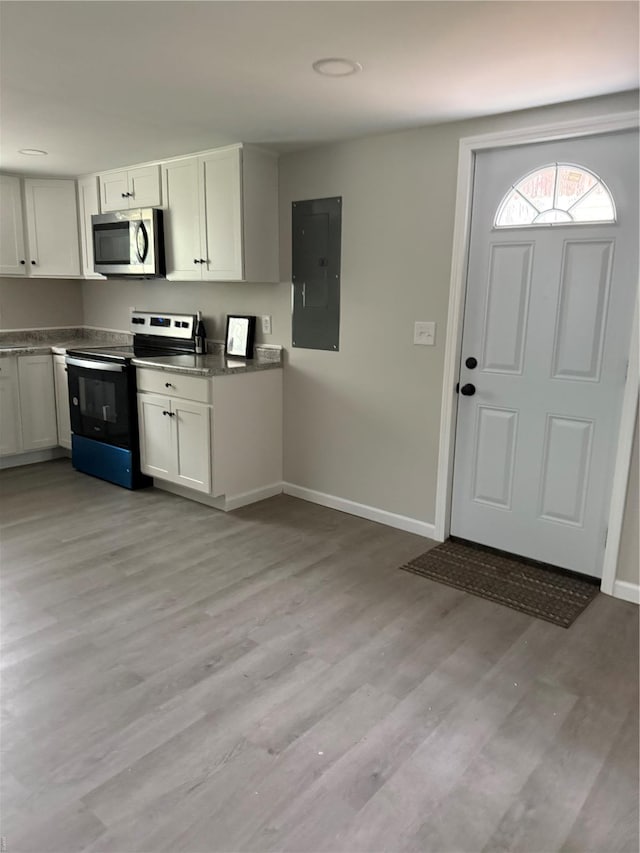 kitchen with baseboards, light wood-style floors, electric panel, white cabinets, and appliances with stainless steel finishes