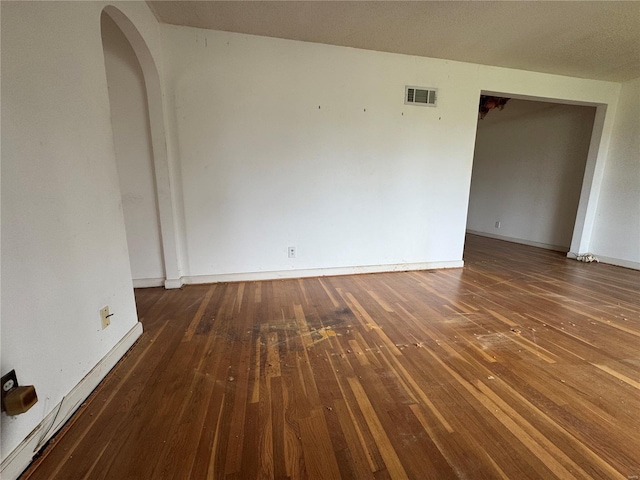spare room featuring arched walkways, baseboards, visible vents, and hardwood / wood-style floors