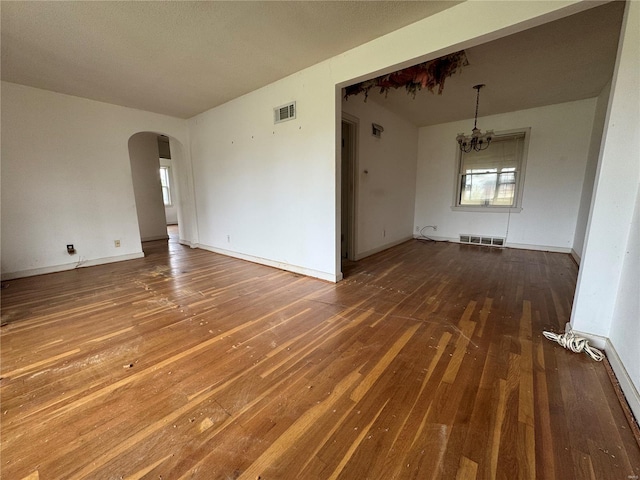 spare room featuring wood-type flooring, a chandelier, and visible vents