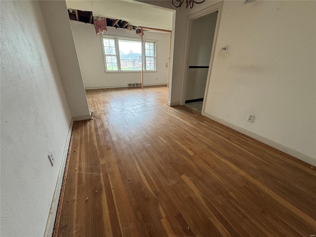 unfurnished room featuring visible vents, baseboards, wood finished floors, and a notable chandelier