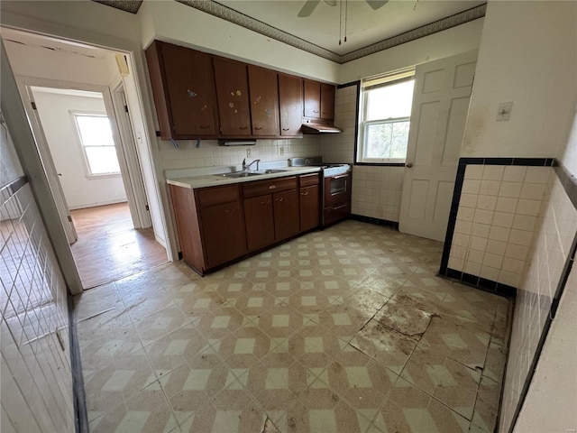 kitchen featuring a sink, tile walls, light countertops, under cabinet range hood, and white gas range oven