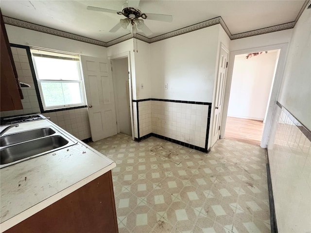 kitchen featuring a ceiling fan, tile walls, wainscoting, a sink, and light floors