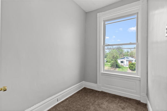 unfurnished room featuring baseboards, plenty of natural light, and dark carpet