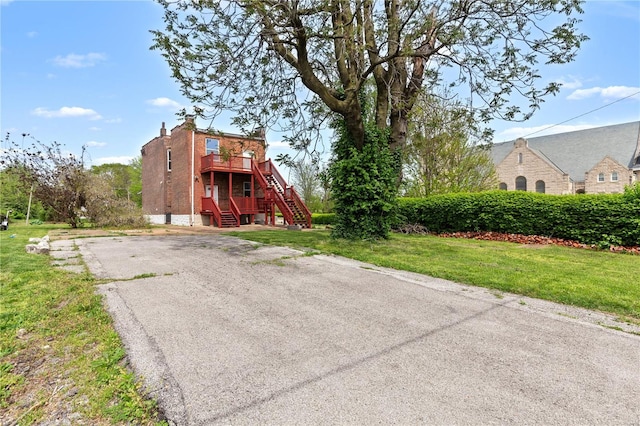 view of front of property featuring stairs, a front lawn, a wooden deck, and driveway