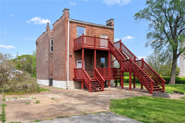 back of house with brick siding, a wooden deck, stairway, a chimney, and a lawn
