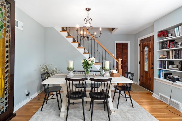 dining space featuring visible vents, an inviting chandelier, wood finished floors, and stairway