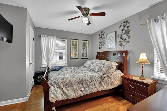 bedroom with baseboards, a ceiling fan, wood finished floors, and multiple windows