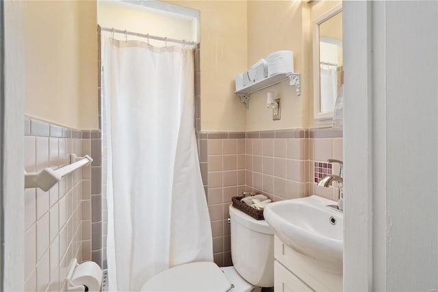 bathroom featuring tile walls, wainscoting, curtained shower, vanity, and toilet