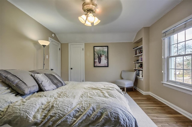 bedroom featuring baseboards, multiple windows, wood finished floors, and lofted ceiling