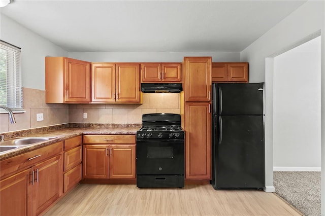 kitchen with a sink, black appliances, light wood-style flooring, and under cabinet range hood