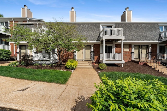 view of front of property featuring a shingled roof, a chimney, mansard roof, and brick siding